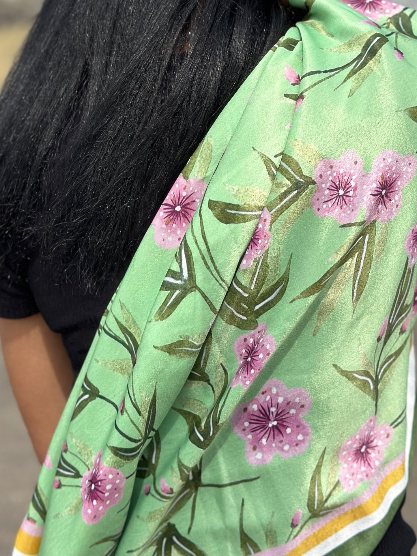 Person with long black hair wearing a green floral shawl outdoors.